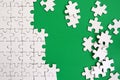 Fragment of a folded white jigsaw puzzle and a pile of uncombed puzzle elements against the background of a green surface. Texture