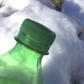 Fragment of garbage green plastic bottle in nature, in the snow, green plastic cap Royalty Free Stock Photo