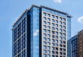 A fragment of the glass facade of a modern concrete building under construction with a reflection of the blue sky and a tower Royalty Free Stock Photo