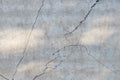 Fragment of gray concrete wall with sun glare and chaotically diverging in different directions, spalls, chips and cracks.