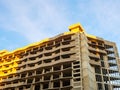 Fragment of a gray wide building under construction, partially illuminated by bright sunlight against a blue sky Royalty Free Stock Photo