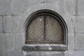 fragment of a historic stone building with a small arched window frame. Old arch window with grille. Bars on the windowframe. grey