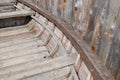 Fragment of inside of port side of an old wooden boat with plank floor, benches and stiffeners leaning against wooden log fence Royalty Free Stock Photo