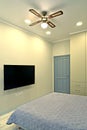 A fragment of the interior of a bedroom with a flat TV on the wall and a chandelier-fan on the ceiling