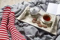 Fragment of legs in red striped socks. interior and home coziness concept. Top view. A cup of tea, a teapot with herbal tea, sugar Royalty Free Stock Photo