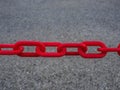 Fragment of a metal chain of red color on the background of grey asphalt. Royalty Free Stock Photo