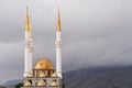 A fragment of a mosque with white minaret towers and gilded domes. The background of the mountain in fog. Copy space.