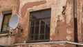 A fragment of an old building with a round satellite dish on the wall. Windos on rear facade of house. Royalty Free Stock Photo