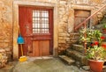 A fragment of an old courtyard with a wooden door and window, cleaning equipment, a stone staircase and a flower pot. Croation.