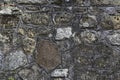 Fragment of old gray stone wall made of different form and size rocks with green moss on it.