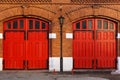 A fragment of an old red brick building with two bright red gates and a street lamp. A unique background for choosing two options Royalty Free Stock Photo