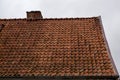 Fragment of old shabby brown beige gable tiled roof of old house with a brick chimney stack furnace with a rain gutter under it