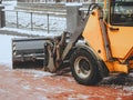 Fragment of orange bulldozer raking snow from tiles