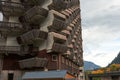 A fragment of the original building with a wooden honeycomb facade with many balconies, against a fall landscape backdrop.