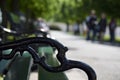 Fragment of park bench with black forged ornate handles. The wooden base of old bench is painted green. Close-up. Selective focus