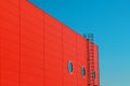 A fragment of a red modern facade of an industrial building, warehouse or shopping center with a round window and a long metal Royalty Free Stock Photo