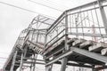 Fragment of staircase of pedestrian bridge over railway. Rusty metal floors. Lines of electrical wires are drawn against gray sky