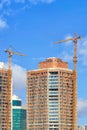 Tower cranes are anchored to modern residential buildings under construction against a blue sky background Royalty Free Stock Photo