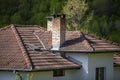 A fragment of a tiled roof with a chimney and windows in a new house in the woods. Royalty Free Stock Photo