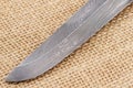 Fragment of the traditional handmade Finnish knife blade with the abstract wave pattern of damascus steel over an old sack backgro