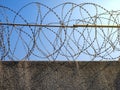 Fragment of the wall with barbed wire in sunlight against the blue sky. Royalty Free Stock Photo