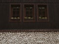 Fragment of a wall of an old brown wooden house with three windows and a stone basement. Royalty Free Stock Photo