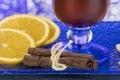 Fragment of a warming drink with cinnamon, orange and ginger on a blue glass surface.