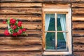 A fragment of a wooden alpine house. The wall made of logs, window and red flowers hanging on the wall Royalty Free Stock Photo