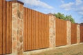 Fragment of a wooden brown modern fence with columns finished with stone , close-up. Modern Style Design wooden Fence Ideas Royalty Free Stock Photo