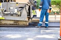 Fragment of applying fresh asphalt in the work of an asphalt paver on the road on a summer day