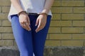 Fragment of a young criminal girl`s body with hands in handcuffs against a yellow brick wall background