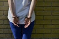 Fragment of a young criminal girl`s body with hands in handcuffs against a yellow brick wall background
