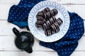 Fragrant cookies of choux pastry in dark chocolate covered with white decoration on a white plate and teapot on a wooden backgroun Royalty Free Stock Photo