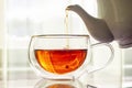 Fragrant strong tea pours from teapot spout in cup on table