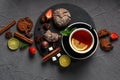 Fragrant tea in a black cup on a black plate with biscuits, lemon, cinnamon and fruits