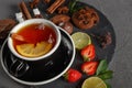 Fragrant tea in a black cup on a black plate with biscuits, lemon, cinnamon and fruits Royalty Free Stock Photo
