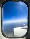 Frame of an airplane window overlooking the mountainous landscape and blue sky, one of the engines and part of the wing in the Royalty Free Stock Photo