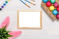 A frame, bunny ears, a flower pot with artificial green grass, colorful eggs in a cardboard box, paints and brushes. Easter Royalty Free Stock Photo