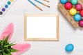 A frame, bunny ears, a flower pot with artificial green grass, colorful eggs in a cardboard box, paints and brushes. Royalty Free Stock Photo