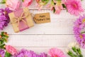 Frame of flowers with Mothers Day gift and tag against white wood Royalty Free Stock Photo