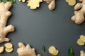 Frame of fresh ginger with green leaves on dark background, flat lay. Space for text