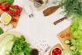 Frame of fresh green salad, red paprika, cherry tomato, pepper, oil and kitchenware on soft white wooden board. Royalty Free Stock Photo