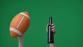 In frame on green background, chromakey female hands with manicure holding an American soccer ball and a glass bottle of Royalty Free Stock Photo