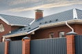 Frame house under construction with a gutter system on a metal roof. Brick chimney pipe. Automatic metal gates.