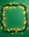 Frame made with Christmas lights on green background, top view. Royalty Free Stock Photo