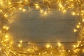 Frame made of Christmas lights on white wooden background, top view. Space for text Royalty Free Stock Photo