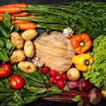 Frame made of fresh assorted vegetables on dark black background around wooden cutting board Royalty Free Stock Photo