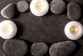 Frame made out of and black round smooth zen stones on black rough flat stone with white spa candles.