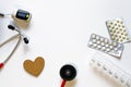 Frame of medical instruments, pills, stethoscope, pulse oximeter, wooden heart, pills blisters and container on white background