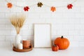 Frame mockup in cozy fall home interior with Halloween decor, pumpkins, vase of dried wheat, candle, coffee cup. Autumn mood,